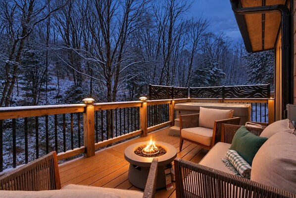 A deck with outdoor seating, a fire pit, and a view of a snowy forest.