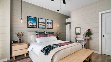 A bedroom with a bed, bedside tables, a bench, a ceiling fan, wall-mounted lights, and framed pictures.