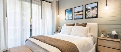 A bedroom with a bed, bedside tables, a bench, and a view of the outdoors.