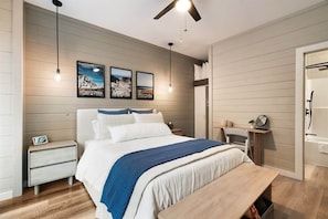 Une chambre à coucher comprenant un lit, des tables de chevet, un banc, un ventilateur de plafond et des lampes fixées au mur.