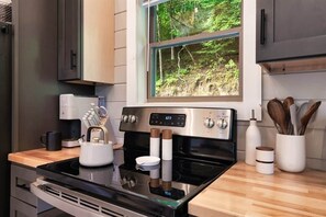 Eine moderne Küche mit Einbauherd, einer Kaffeemaschine und einem Fenster mit Blick auf einen Wald.