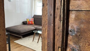 Quarto com vigas de madeira aparentes, um sofá, uma mesa pequena e uma mesa de centro de vidro.