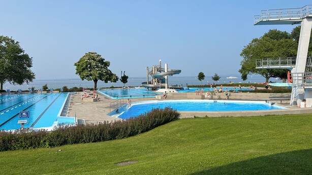 Um complexo de piscinas com várias opções e um toboágua, rodeado por gramados verdes e árvores.