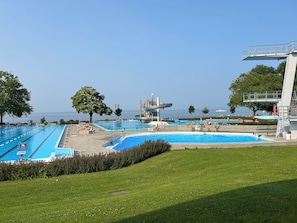 A swimming pool complex with multiple pools and a water slide, surrounded by green lawns and trees. - Charming vacation apartment on the lakefront (Arbon)