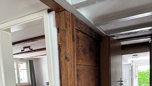 Quarto com piso de madeira, cama com cobertor vermelho e janela com cortinas.