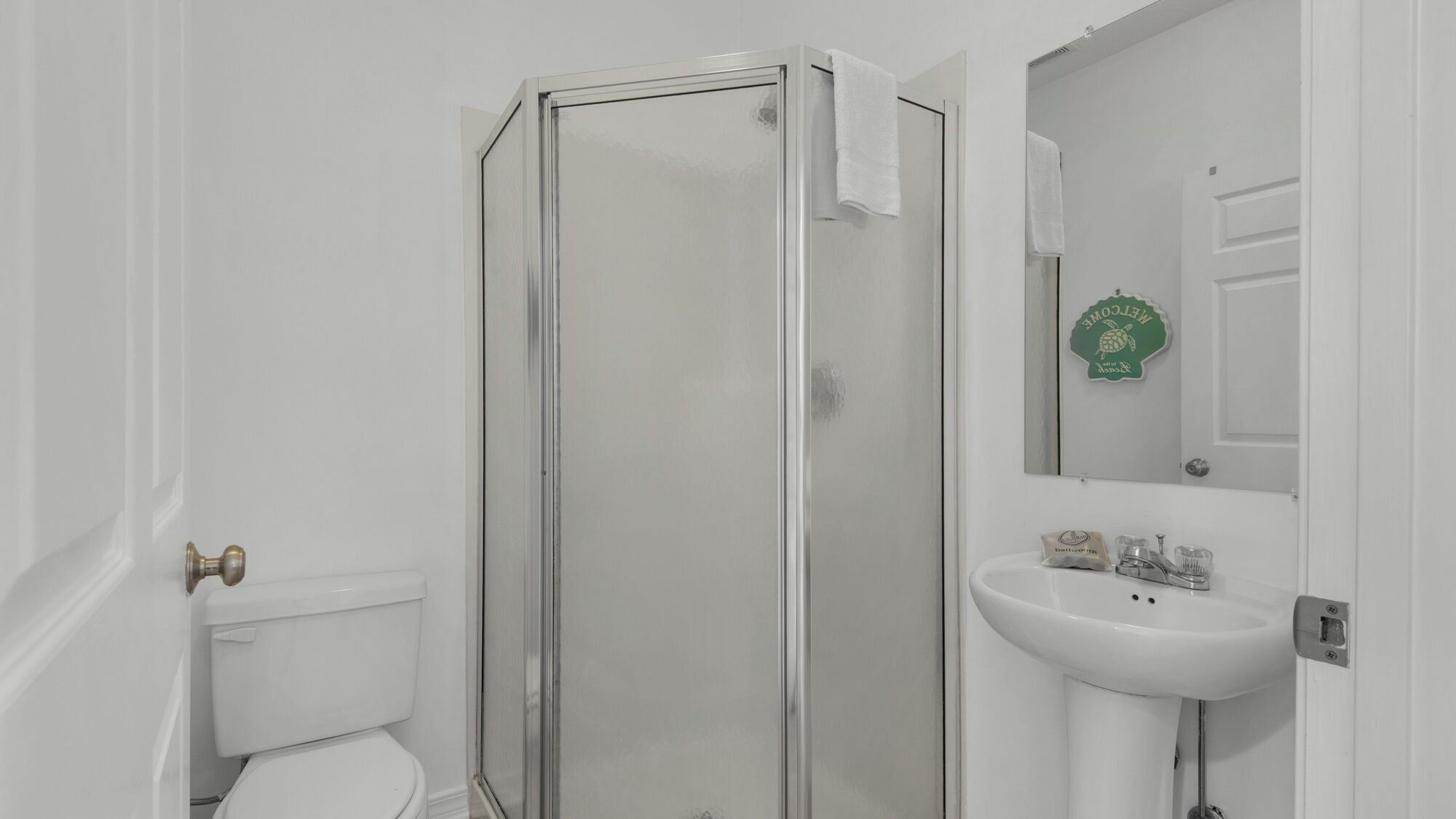 Une salle de bain comprenant des toilettes, une douche fermée par des parois de verre et un lavabo avec un miroir au-dessus.
