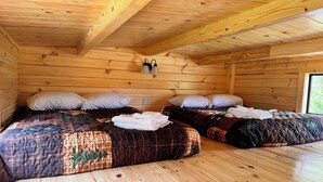 Una baita di legno con due letti, ognuno con copripiumino trapuntato e cuscini.