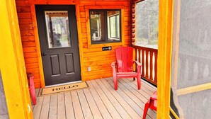 Una baita di legno con un portico, una sedia rossa e un ingresso con lo zerbino 'HELLO'.