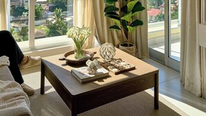 Amplia habitación con ventanas grandes, una mesa de centro de madera, una planta en maceta y vistas de la ciudad.