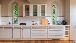Una cocina moderna con armarios blancos, encimera de madera y vistas a través de ventanales arqueados.