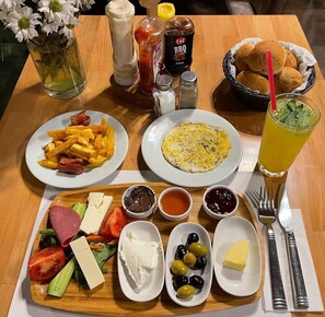 A meal with fries, eggs, salad, cheese, olives, and condiments on a wooden table. - Mitani Suites (Istanbul)