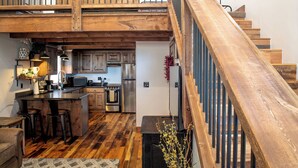 A spacious kitchen with wooden flooring, a central island with bar stools, stainless steel appliances, and a wooden staircase.