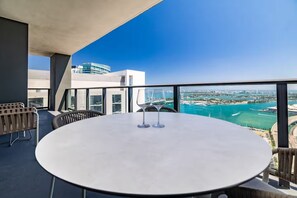 Mesa redonda com duas taças de vinho em varanda com vista para a paisagem urbana e o mar.