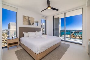 Quarto moderno com uma cama grande, um ventilador de teto e vista para a cidade através de janelas do chão ao teto.
