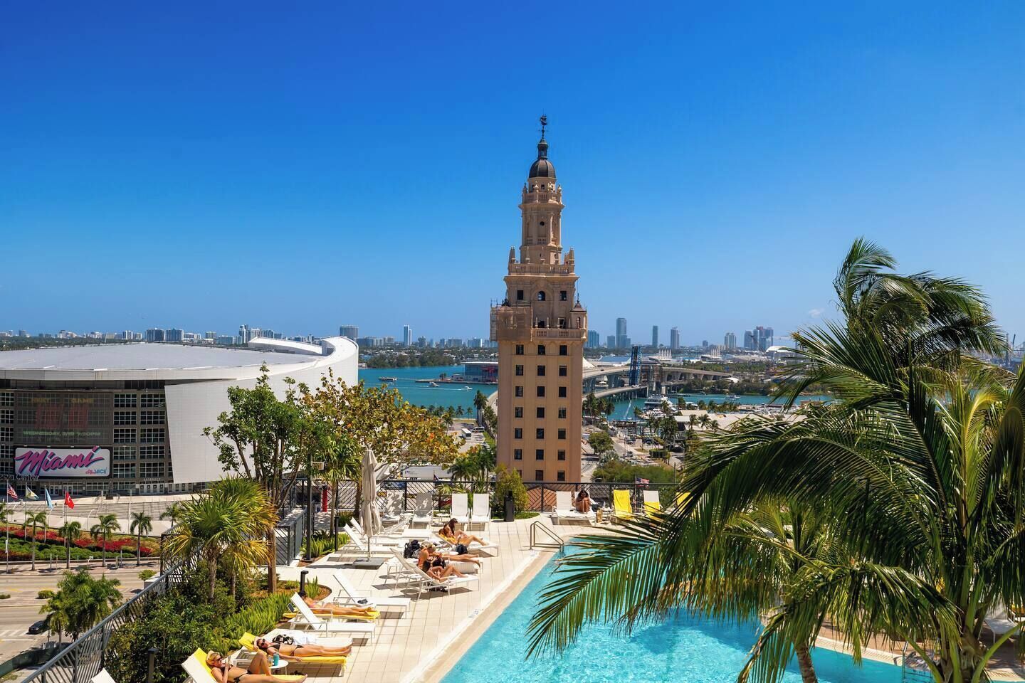 A hotel with a pool, palm trees, and a view of a city skyline.