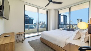 A modern hotel room with a large bed, a desk, a chair, a TV, and a balcony with a city view.