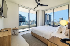 Una habitación de hotel moderna con una cama grande, un escritorio, una silla, un televisor y un balcón con vistas a la ciudad.