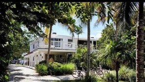 A two-story building with a covered porch and a pathway leading to it, surrounded by lush greenery and palm trees. - Islamorada Suite With Kayaks •Patio & Garden Views - Wildflower Suite (Islamorada)