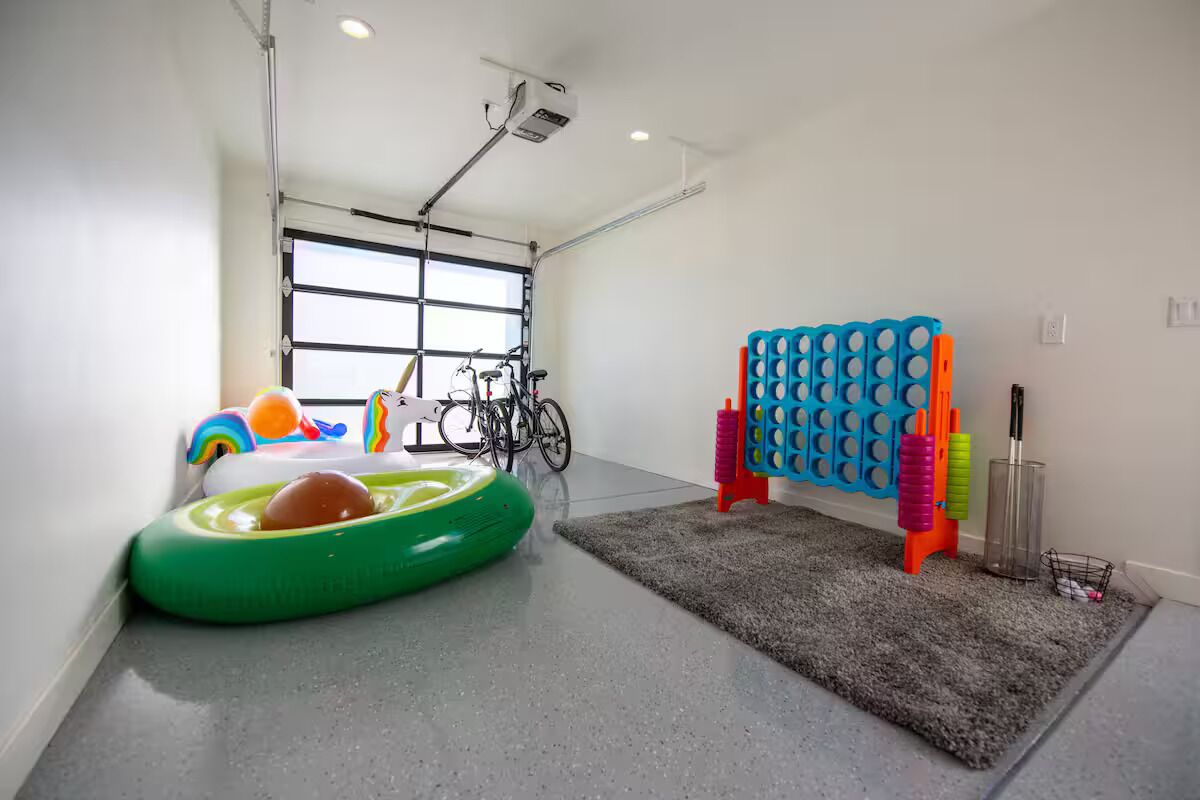 A room with a grey carpet, a green inflatable pool, a bicycle, and a blue and orange play structure.