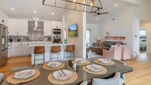 A modern kitchen with white cabinets, a central island, and a dining area with a glass table and woven placemats.