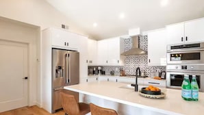 A modern kitchen with white cabinetry, stainless steel appliances, a central island with bar stools, and decorative backsplash tiles.