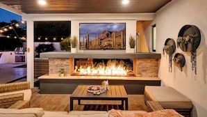 A modern outdoor living area with a fireplace, seating, and decorative wall art.