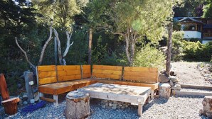 A wooden bench with a built-in table, surrounded by trees and a gravel path.