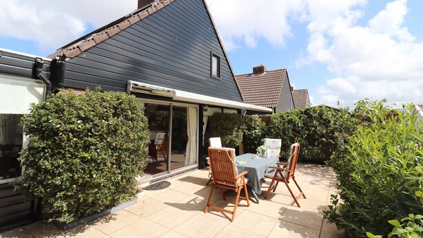 A house with a dark roof, a patio with a table and chairs, and a garden area with bushes. - Holiday Home in Noordwijkerhout by Forest & Lake (Noordwijkerhout)