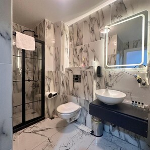 A bathroom with a glass shower enclosure, a toilet, a sink with a mirror, and marble tiles. - Cetinkaya Suites (Istanbul)