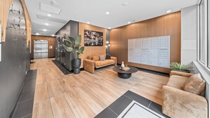 A modern lobby with a wooden floor, a sofa, a coffee table, a potted plant, a wall-mounted art piece, and a row of lockers. - King Bed & Rooftop Views Prime Bankers Hill near Balboa Park (San Diego)