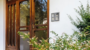 A wooden door with glass panels, a small outdoor mat, and a wall-mounted device. - De Vivo Realty - Lunamare Sorrento (Sorrento)