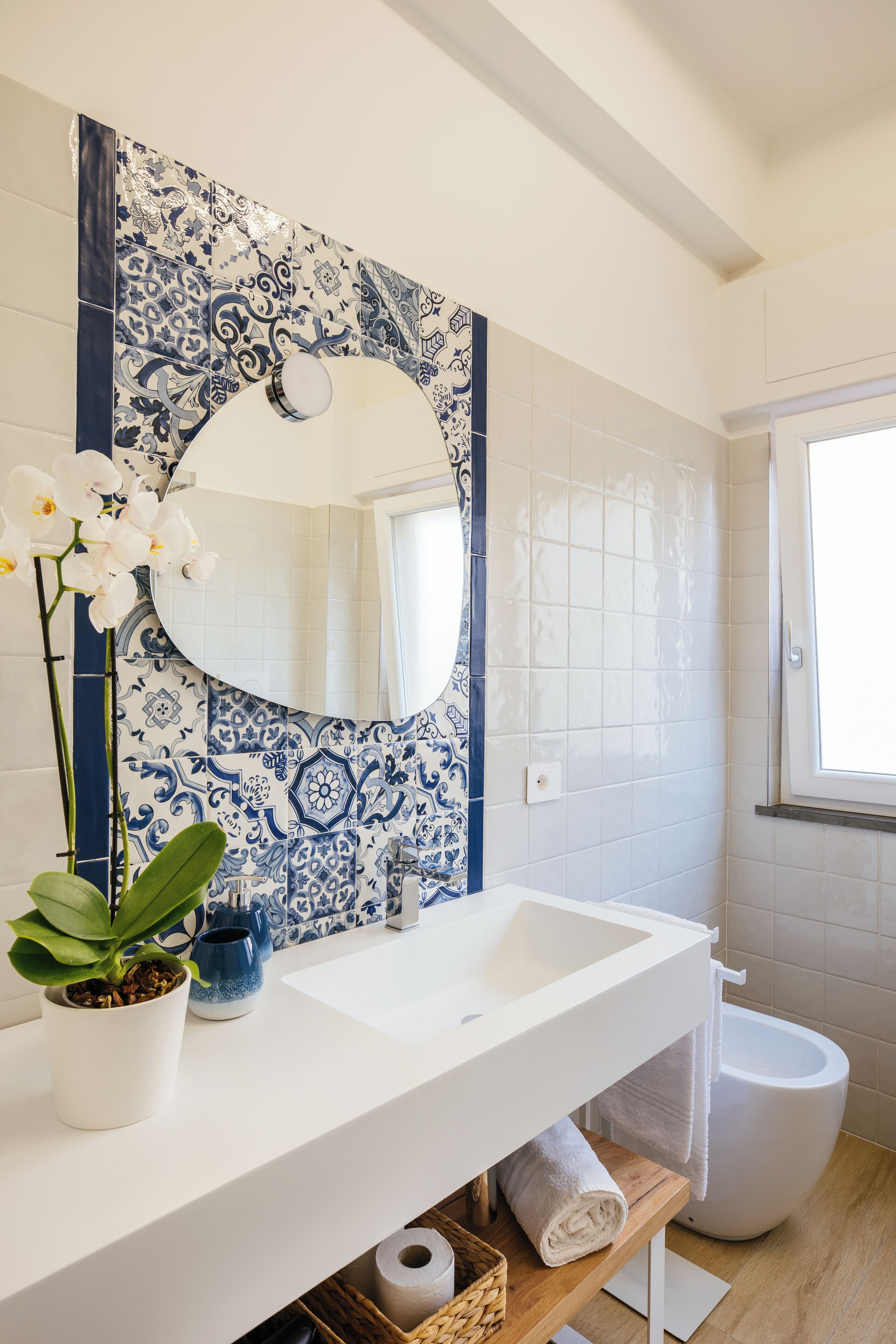 A bathroom with a white sink, blue and white patterned tiles, a potted plant, a mirror, and a toilet.