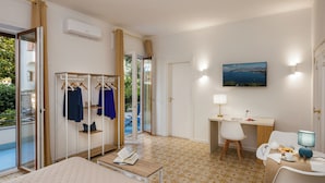 A hotel room with a bed, a desk with a chair, a wardrobe, and a view of the outdoors. - De Vivo Realty - Lunamare Sorrento (Sorrento)