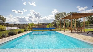 A rectangular swimming pool with clear blue water, surrounded by a wooden deck and a pergola with chairs. - Modern country house - sleeps 8/10 - heated pool (Tarabel)