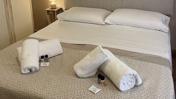A neatly made bed with a patterned bedspread, a bedside lamp, and toiletries on the bed. - Vacation Home Balai Porto Torres (Porto Torres)