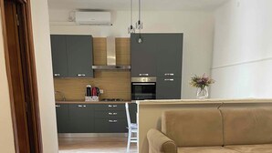 A modern living room with a dark wooden table, a beige sofa, and a kitchen in the background. - Vacation Home Balai Porto Torres (Porto Torres)