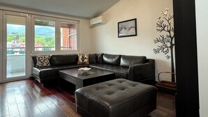 Ein modernes Wohnzimmer mit einer Ledersofa, einem Couchtisch und einem großen Fenster mit Blick auf Gebäude und Grünflächen.