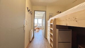 A narrow hallway with wooden flooring, a bunk bed on the right, and a door leading to a balcony.