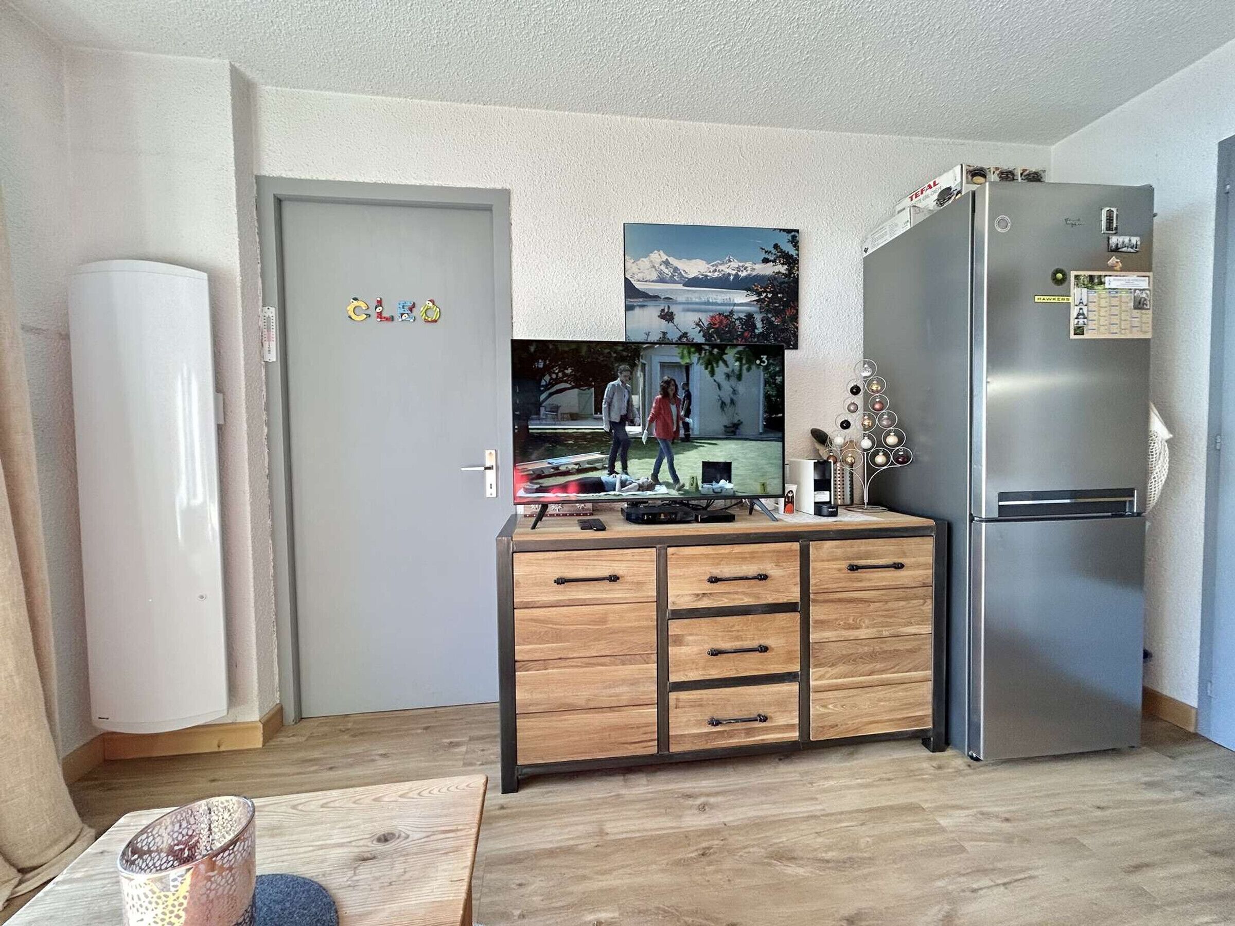 A compact kitchen with a refrigerator, a wooden cabinet with drawers, and a door with a 'GLO' sign.