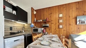 A compact kitchen with a dining area, wooden walls, and a table set for four.