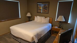 Una habitación de hotel con una cama grande, dos lámparas de noche, un televisor de pantalla plana y un cuadro con un paisaje en la pared.