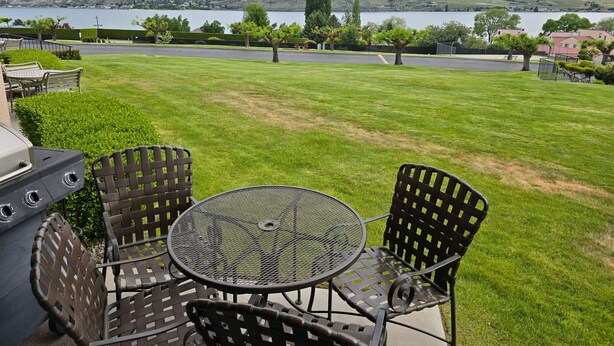 Un patio con una parrilla, sillas y una mesa con vistas a un lago y colinas.