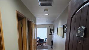 Un pasillo con suelo de baldosas, puertas de madera, una ventana con persianas y una puerta con placa de número.
