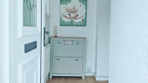 A narrow hallway with a wooden floor, a white door with a glass panel, and a light blue cabinet with a flower painting above it. - Family and pet-friendly flat near beach and countryside (Baglan)