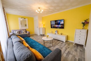 A living room with a sofa, a coffee table, a TV mounted on the wall, and a white cabinet. - Family and pet-friendly flat near beach and countryside (Baglan)