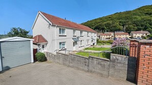 A two-story residential building with a red-tiled roof, a garage, and a small garden area. - Family and pet-friendly flat near beach and countryside (Baglan)