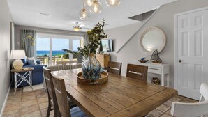 Spiseområde med et træbord, stole, en vase med planter, et fjernsyn og havudsigt.