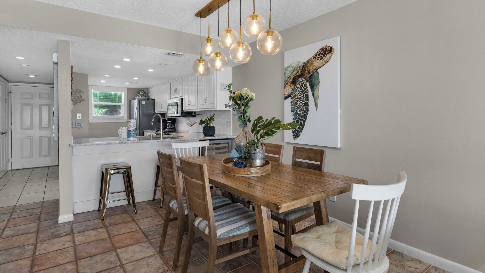 A modern kitchen with white cabinets, a wooden dining table, and a hanging light fixture.