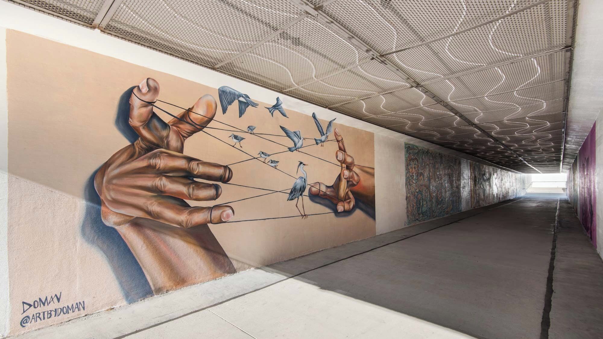 Een tunnel met een muurschildering van een hand die vogels beheerst.