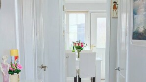Un pasillo que conduce a un comedor con muebles blancos y un jarrón de flores.